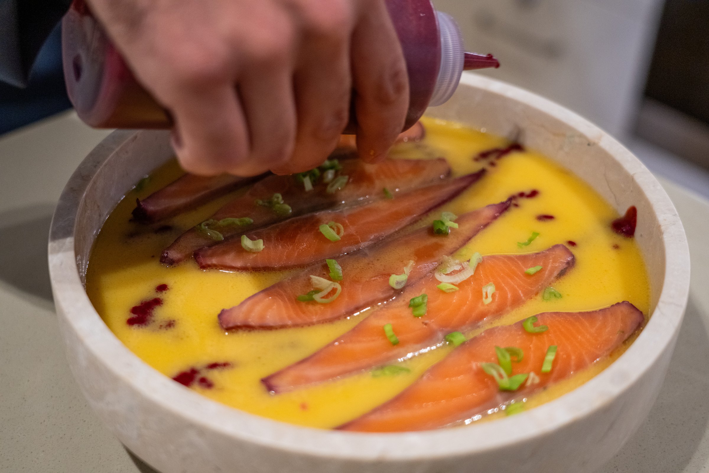 Chef aboard AQUARIUS finishing a plate of cured salmon in citrus broth