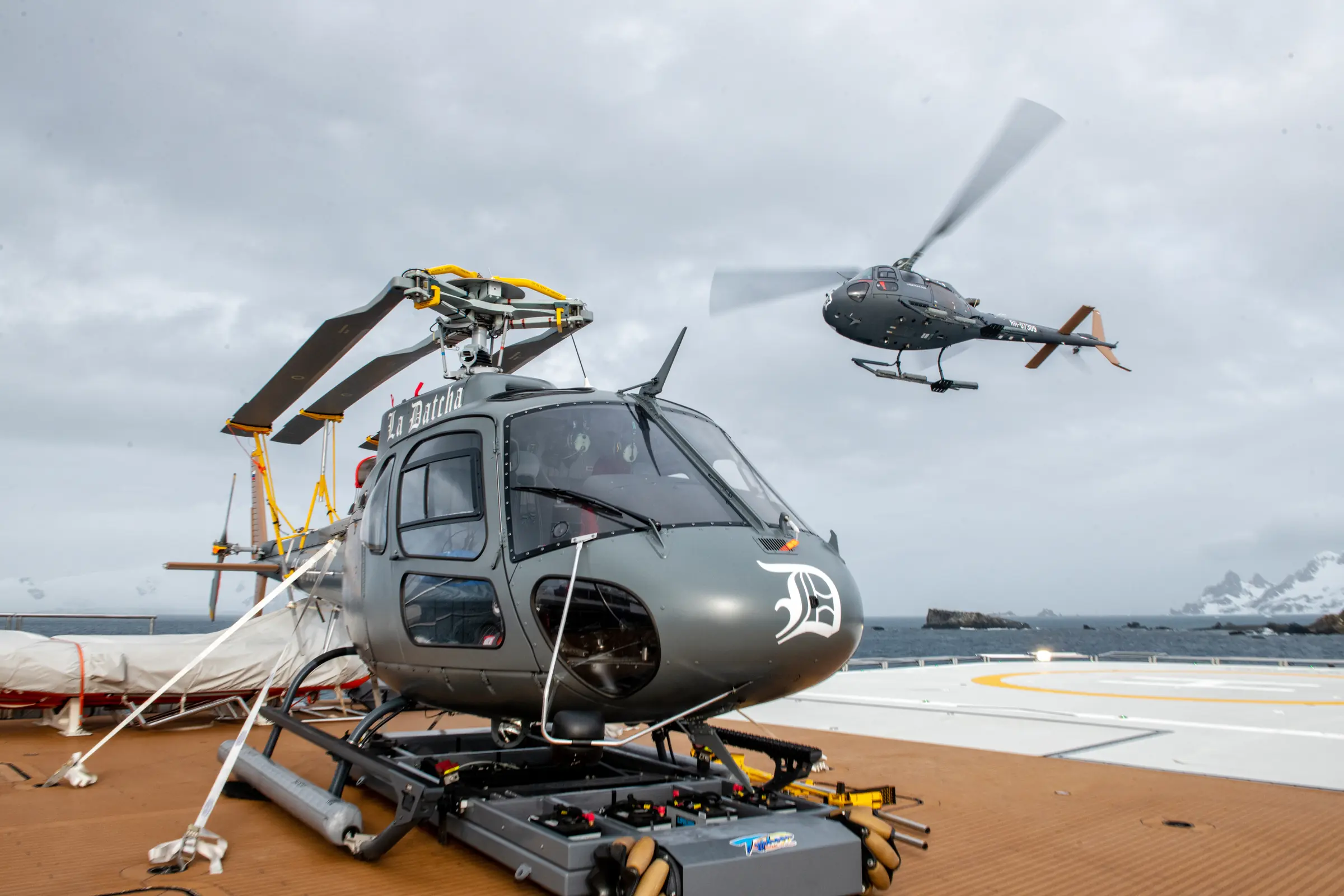 Helicopter secured on LA DATCHA's aft deck while a second aircraft hovers nearby
