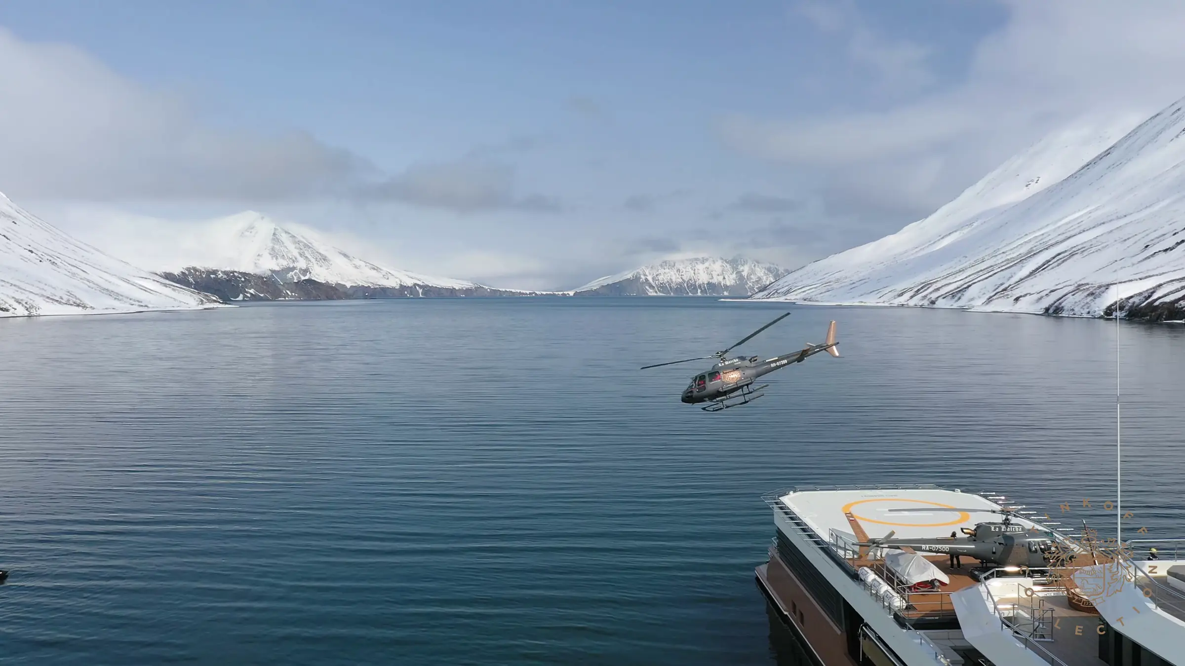 Helicopter flying above LA DATCHA's aft helideck in a snow-covered fjord