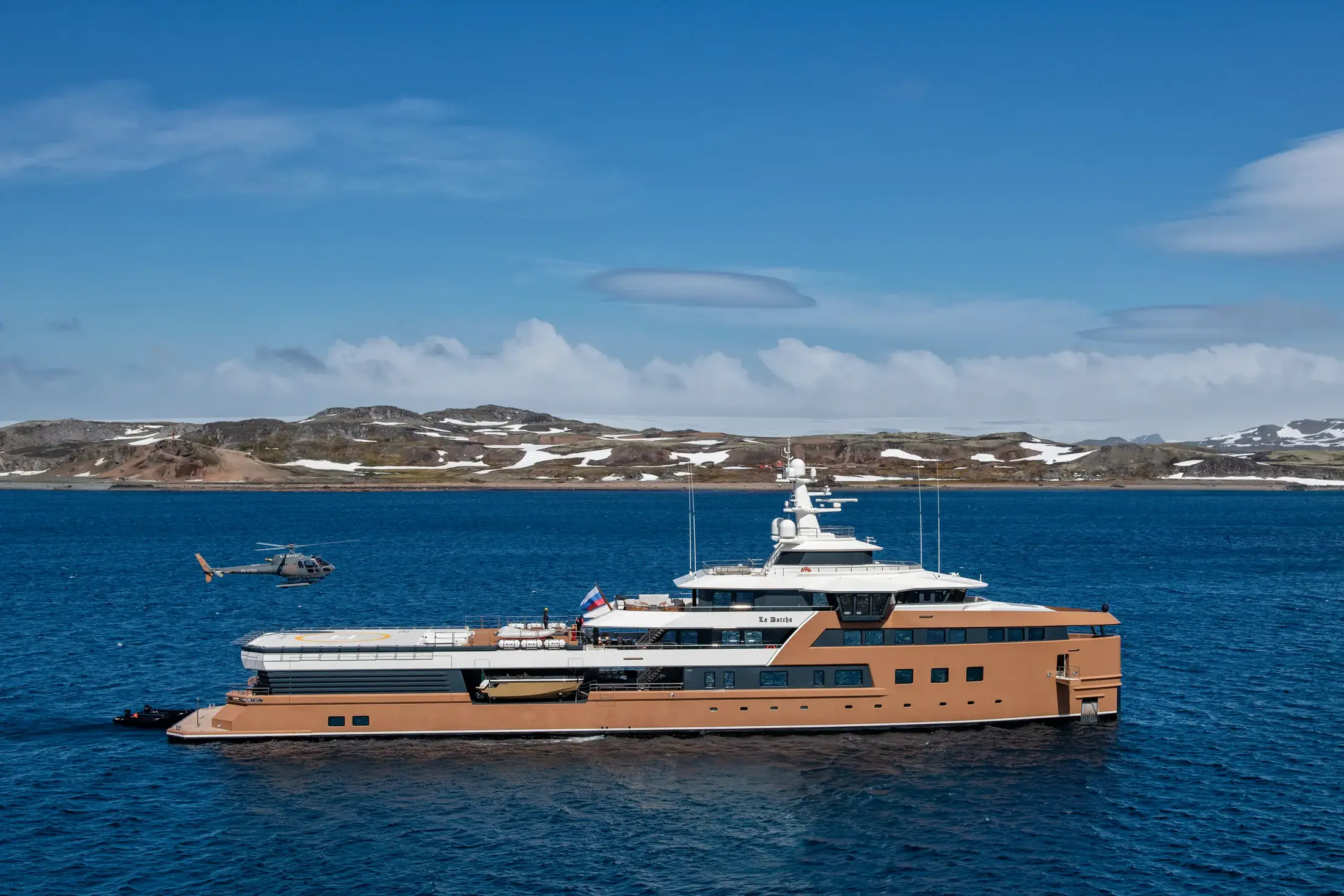 LA DATCHA broadside in polar water with a helicopter near a rugged shore
